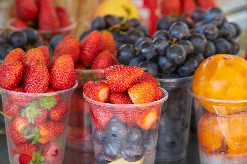 Vibrant strawberries, grapes, and persimmons displayed in plastic cups at a market.